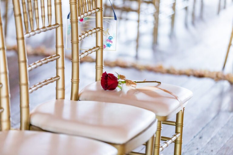 A rental chair in gold and white set in a wedding hall.